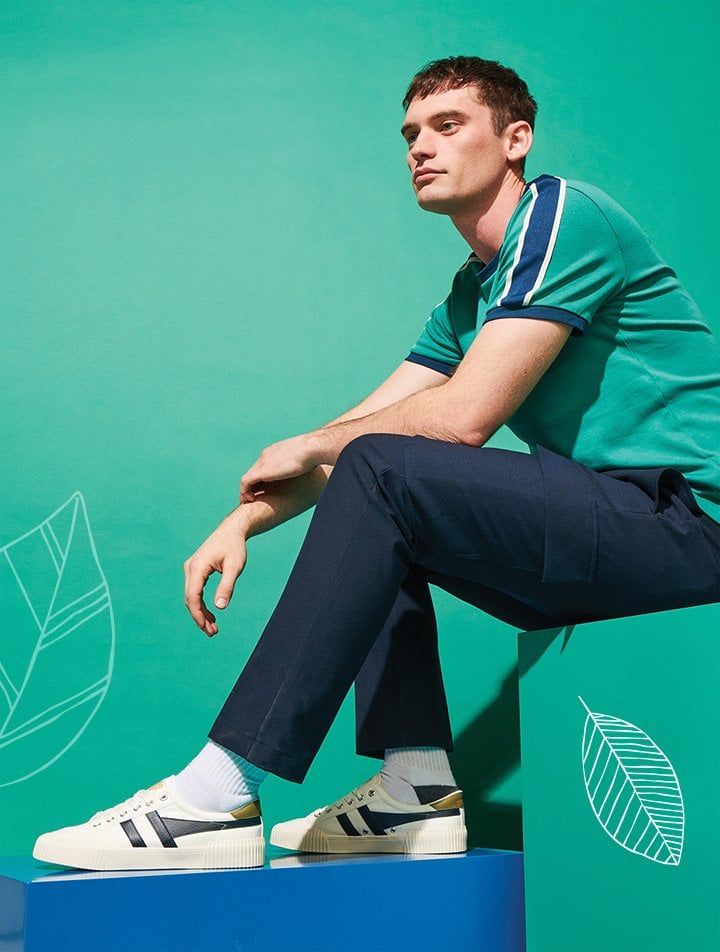 Man in green shirt, navy pants, and white sneakers sitting on blue and green blocks.