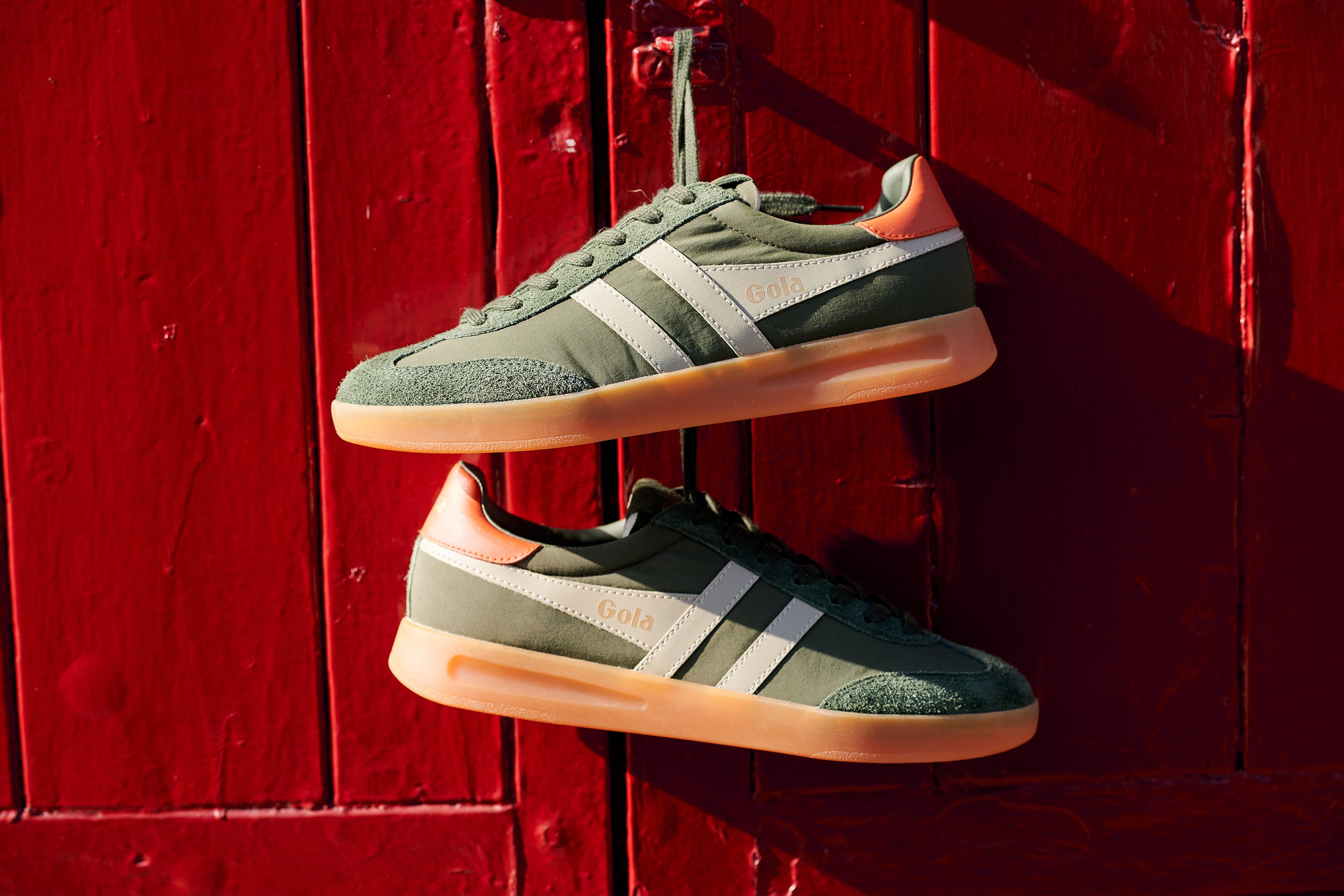 Green trainers with white stripes hanging on a red wooden door